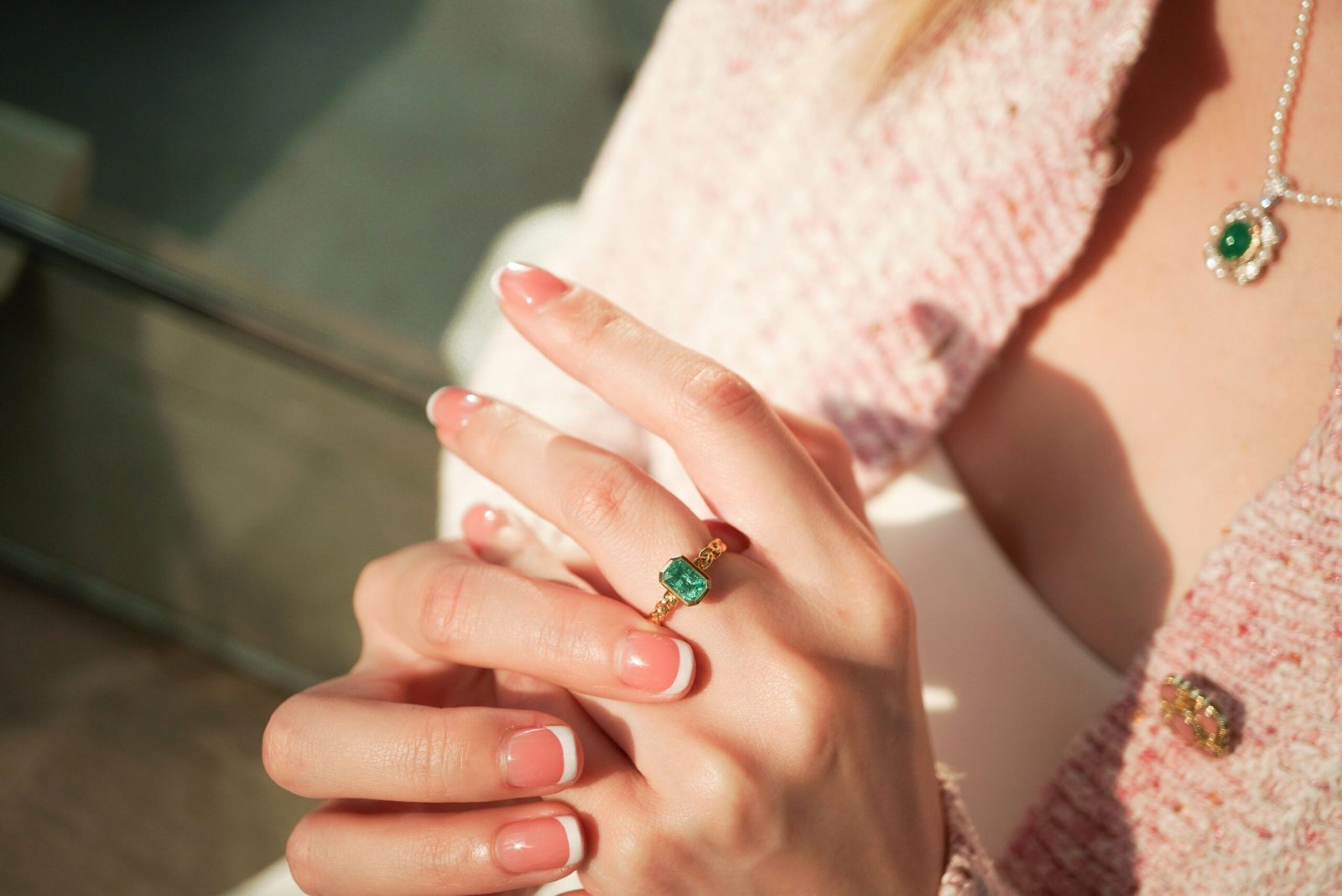 Close-up of elegant hands wearing emerald jewelry with soft lighting.