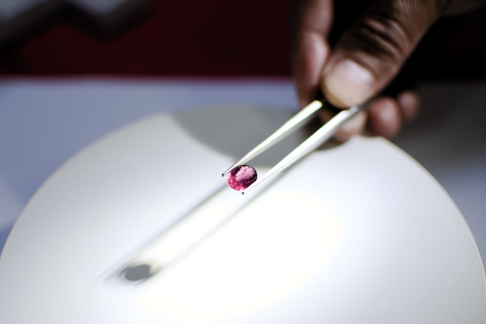Detailed image of a hand holding a red gemstone using tweezers, perfect for jewelry and gemology themes.